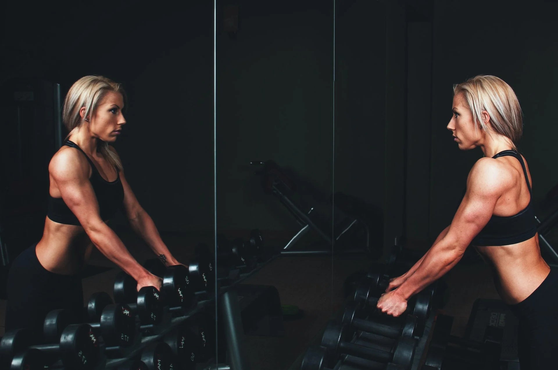 Female athlete strength training with dumbbells in a gym mirror